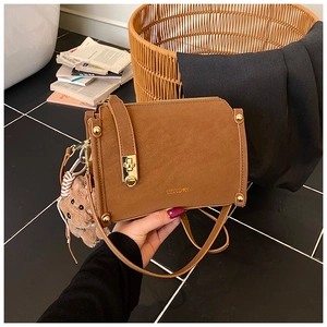 Detail of vintage brown leather bag featuring golden logo and cute bear charm accessory