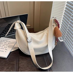 Detail of cream crescent bag with furry pom-pom and silver buckle on dark leather background