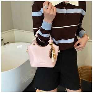 Bolso de mano en cuero rosa con colgante de cuentas y herrajes dorados en una modelo