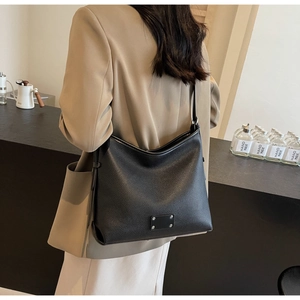 Macro detail of black litchi grain leather tote bag with metal base decor on a casual outfit