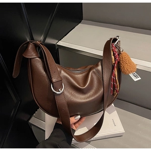 Detail of dark brown faux leather crescent bag with wide strap and plush pendant