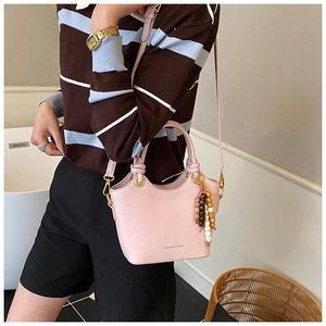 Sac seau rose avec breloque de perles et détails dorés dans un décor intérieur élégant