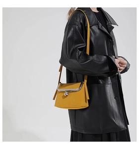 Detail of a mustard yellow mini crossbody bag with metal ball clasp on a black outfit