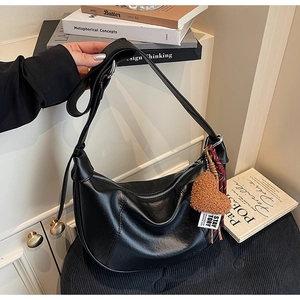Detail of black leather hobo bag with a brown fuzzy heart charm on a stack of books