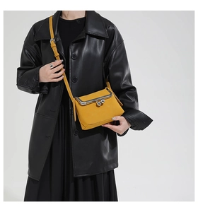 Detail of a bright yellow crossbody bag with silver ball clasp and leather strap on model
