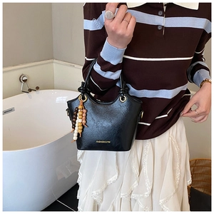 Détail du sac à main en cuir noir avec pompon en perles de bois et logo doré