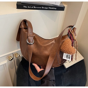 Detail view of a vintage brown leather crescent bag with adjustable strap and heart charm