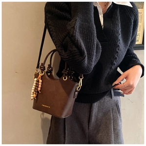 Détail d'un sac seau vintage en cuir marron café avec lettrage de mode et pendentif perlé