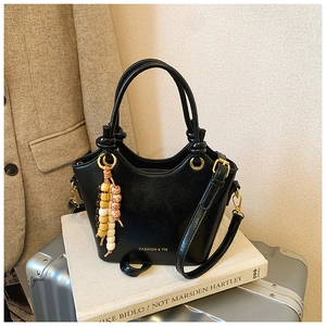 Détail du sac à main noir en cuir PU avec poignée nouée et breloque en perles