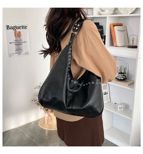 Détail du sac hobo en cuir noir avec décorations d'œillets métalliques sur la bandoulière