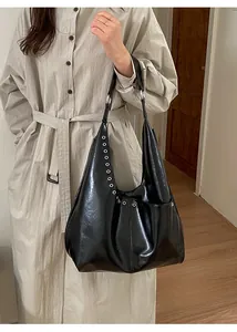Détail du sac hobo noir brillant avec œillets argentés porté par un mannequin en trench