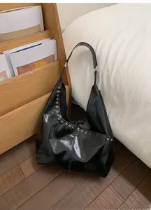 Détail d'un sac Hobo noir avec œillets métalliques argentés posé sur un porte-revues