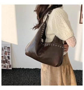 Détail du sac hobo en cuir marron foncé avec œillets argentés porté par un mannequin