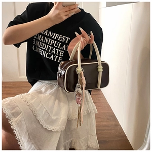 Détail d'un sac Boston marron foncé avec poignées crème et charmant pendentif d'ours