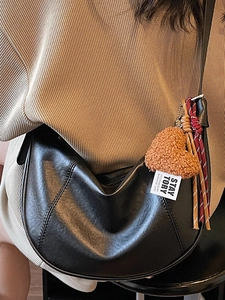 Minimalist black leather half-moon crossbody bag with heart charm and woven strap details