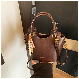 Détail d'un sac à main vintage marron foncé avec pompon en perles et logo