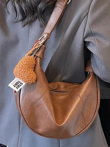 Minimalist caramel brown crescent shoulder bag with plush heart charm and wide strap