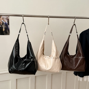 Trois sacs hobo en cuir de grande capacité en noir, beige et marron suspendus sur un rack