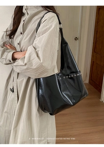 Détail d'un sac cabas noir en similicuir brillant avec œillets métalliques et bandoulière