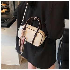 Détail d'un sac Boston blanc crème avec des anses marron et une bandoulière dans un café