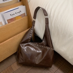 Détail d'un sac hobo en cuir marron foncé brillant avec des œillets métalliques argentés