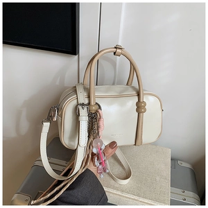 Close-up of cream Boston bag with contrasting brown handles and cute pink doll charm