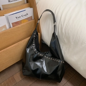 Détail du sac d'épaule noir brillant avec œillets argentés et bandoulière large