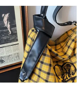 Detail of yellow plaid tote bag with black leather strap and heart-shaped embroidery