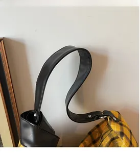 Detail of yellow checkered canvas bag showing black leather straps and silver metal hardware
