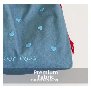 Detailansicht der Denim-Tasche mit hellblauer Herzbestickung und rotem Kordelzug-Detail