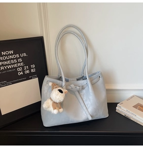 Détail du sac cabas en cuir bleu clair avec boucle décorative et charm de chien en peluche