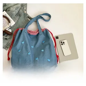 Detail der Denim-Einkaufstasche mit blauer Herzbestickung, rotem Kordelzug und Karofutter