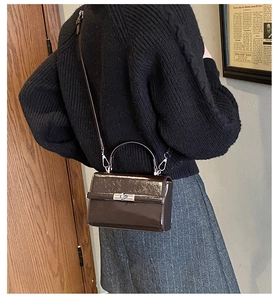Detail of a deep brown patent leather handbag featuring a vintage metal twist lock