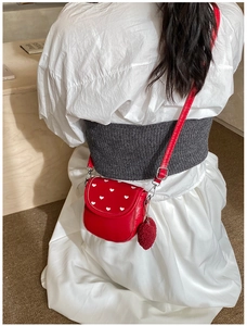 Détail du sac bandoulière rouge avec broderies de cœurs blancs et breloque en peluche