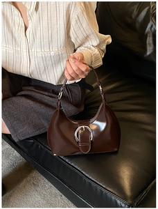 Détail d'un sac demi-lune en cuir verni marron foncé avec une boucle en métal argenté brillant