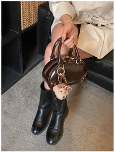 Detail of dark brown glossy leather handbag with gold rivets and cute bear charm