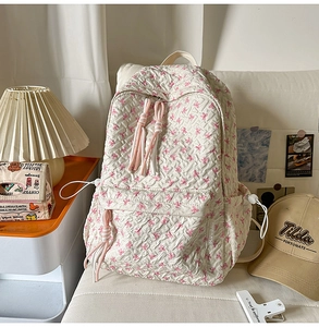 Detail of white quilted backpack featuring pink bow patterns and a decorative long fringe