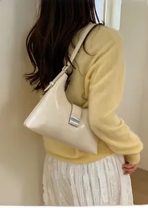 Detail of a creamy white glossy leather hobo bag with a silver buckle worn by a model
