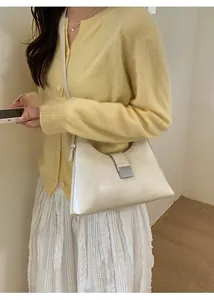 French style cream underarm bag with silver buckle worn over a yellow knit sweater