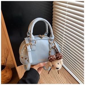 Detailed view of light blue Boston bag featuring a plush bear charm and golden logo detail