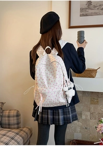 Close-up of lightweight off-white backpack with pink bow pattern and plush bear charm