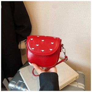 Détail du sac bandoulière rouge à motifs de cœurs avec livre d'art et fond de bagage