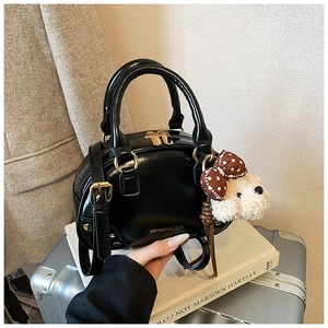Detailed close-up of a black leather handbag with gold hardware and a cute dog plush charm