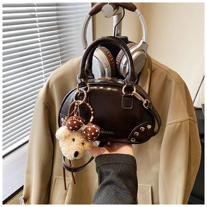 Detail of dark brown glossy square handbag with gold logo and plush bear charm