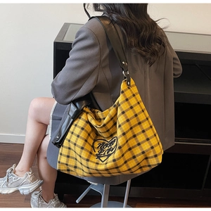 Detail of yellow checkered tote bag with heart embroidery worn by a model in gray blazer
