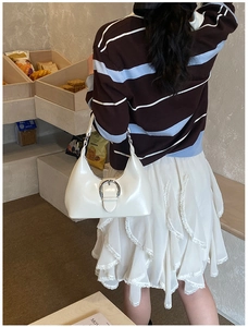 Détail du sac sous le bras blanc brillant avec boucle argentée porté par le mannequin