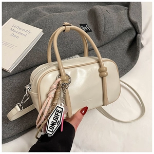 Détail d'un sac Boston crème avec des anses marron clair et un pendentif tissé lettré