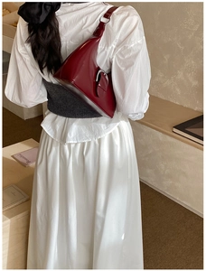 Détail du sac hobo en cuir verni bordeaux avec boucle argentée porté à l'épaule