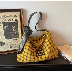Detail of hobo tote bag featuring yellow plaid canvas and black heart embroidery