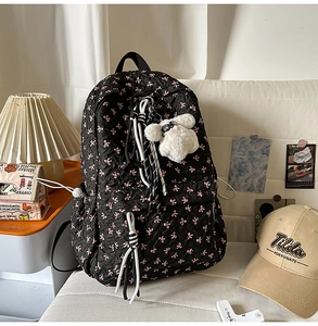 Detail of black quilted backpack with pink bow prints and a white plush toy charm